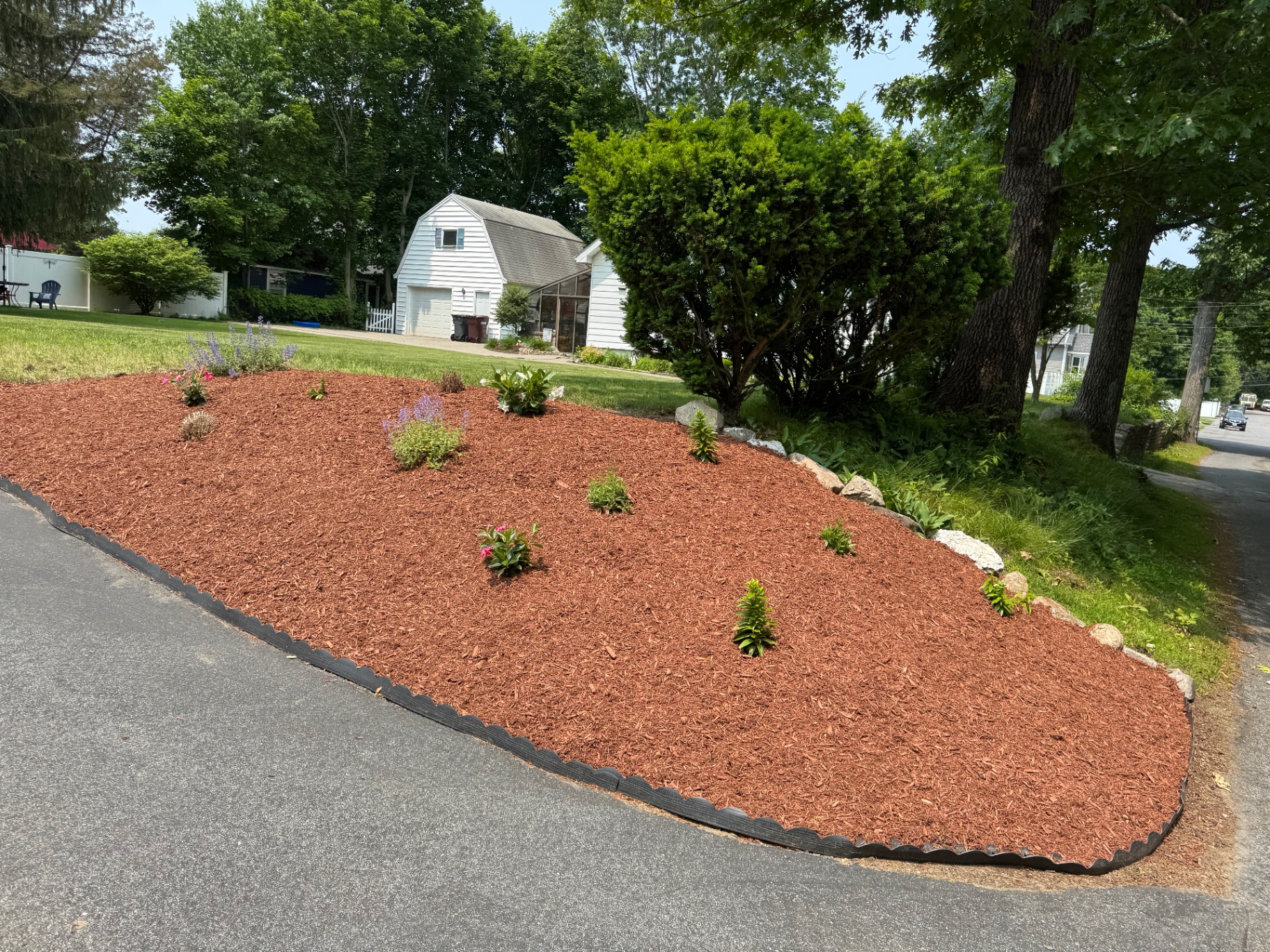 Large driveway island bed with fresh red mulch, perennials, and stone edging