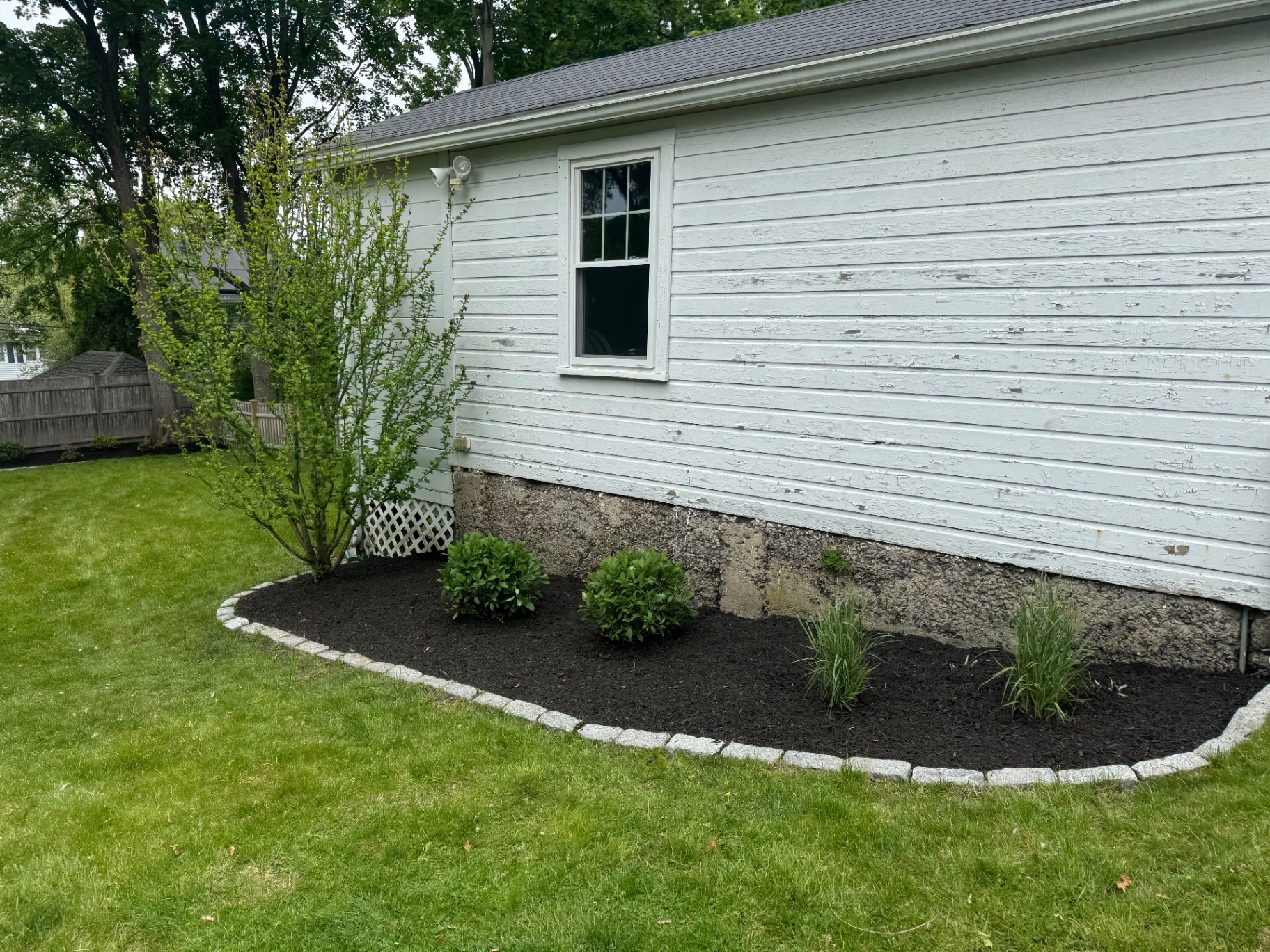 Side-yard foundation bed with shrubs, ornamental grass, and cobblestone edging