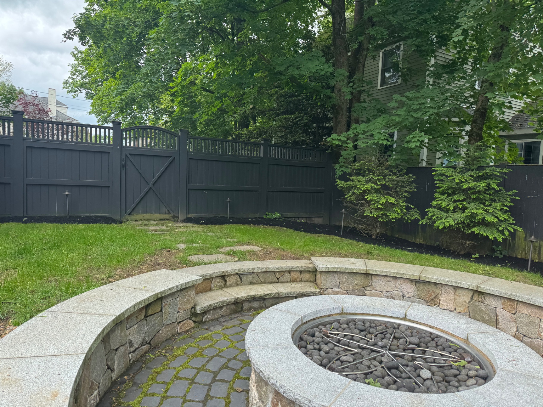 Granite fire pit with curved fieldstone seat wall and cobblestone base