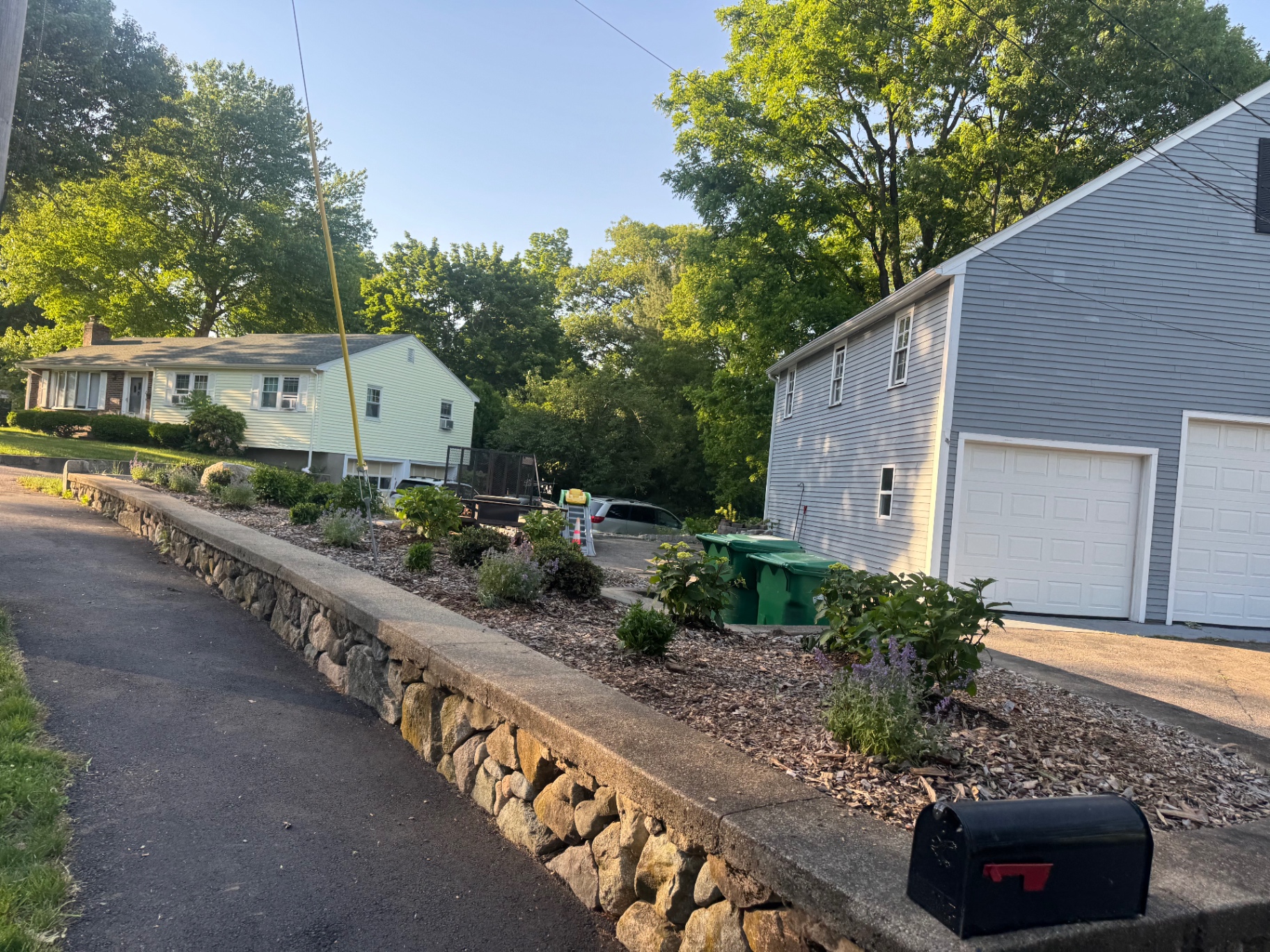 Wide view of a planting bed above a stone retaining wall by a driveway