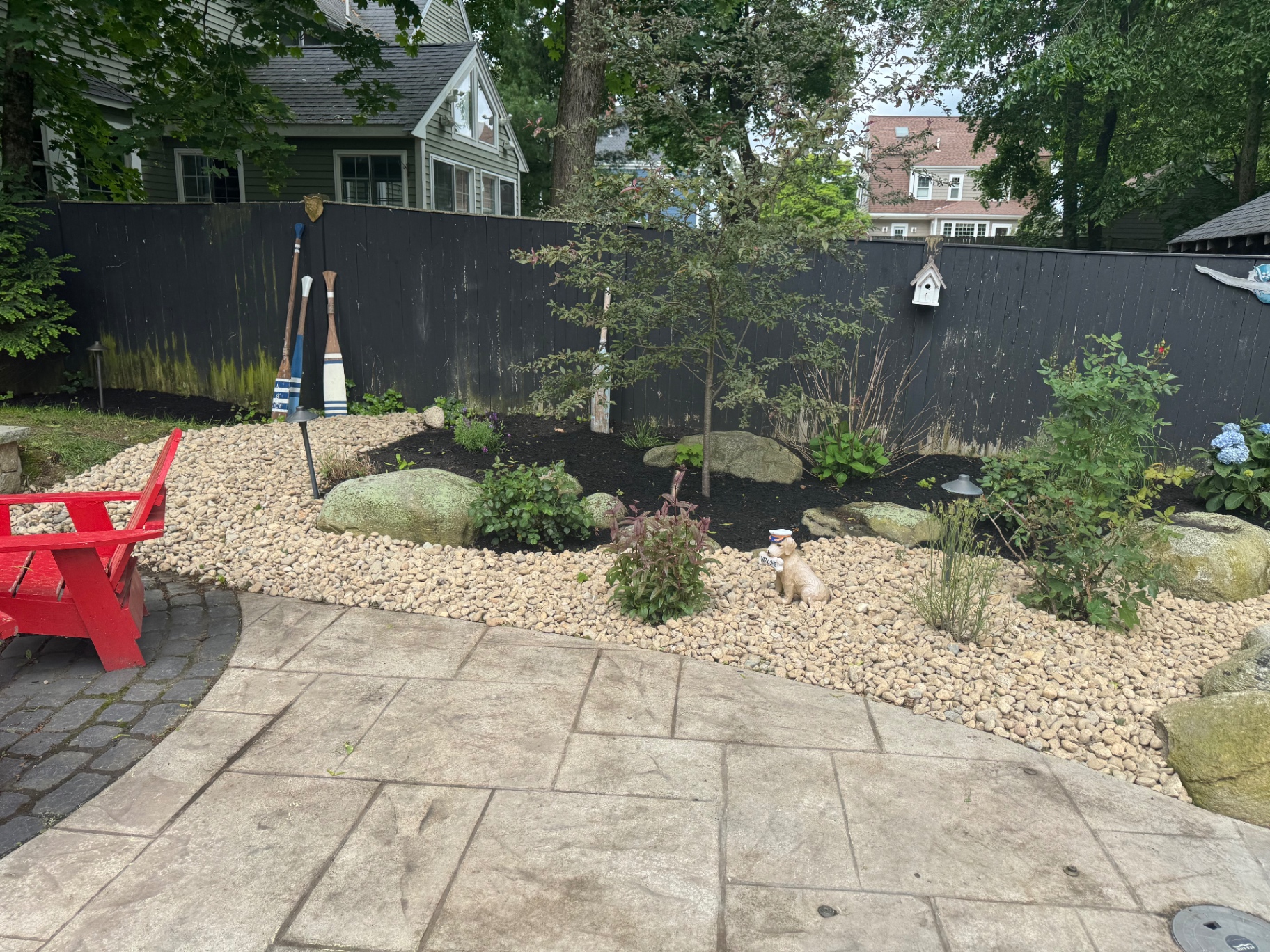Backyard bed with river rock, boulders, and new plantings beside a stamped concrete patio