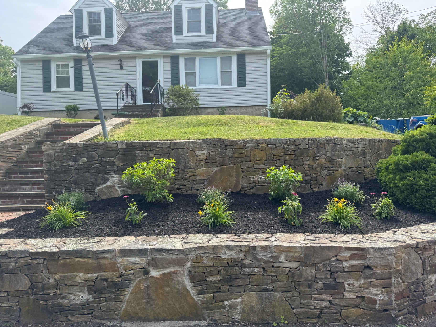 Wide view of tiered stone retaining walls with newly planted front landscape bed