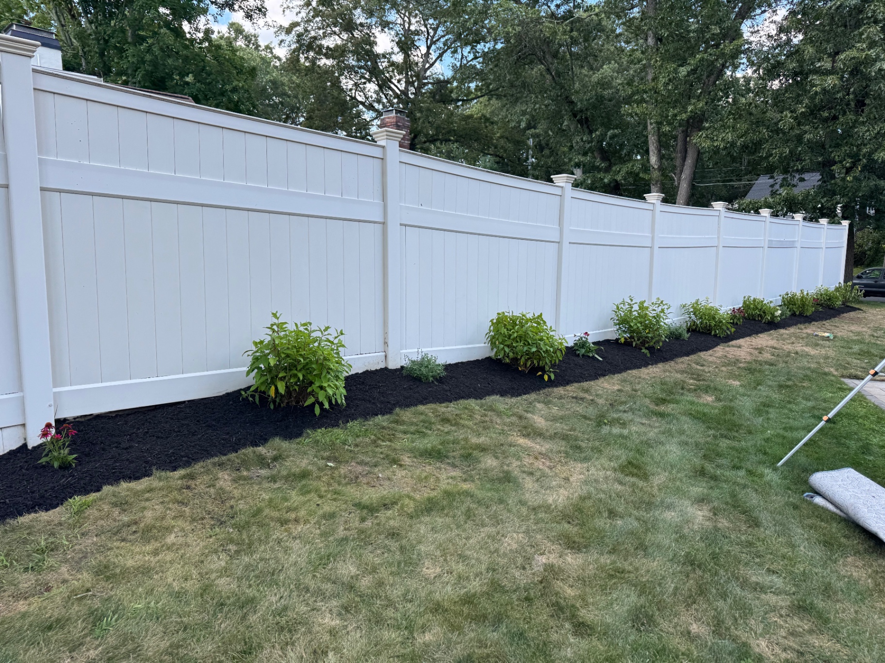 New plantings and mulch bed along a white vinyl fence