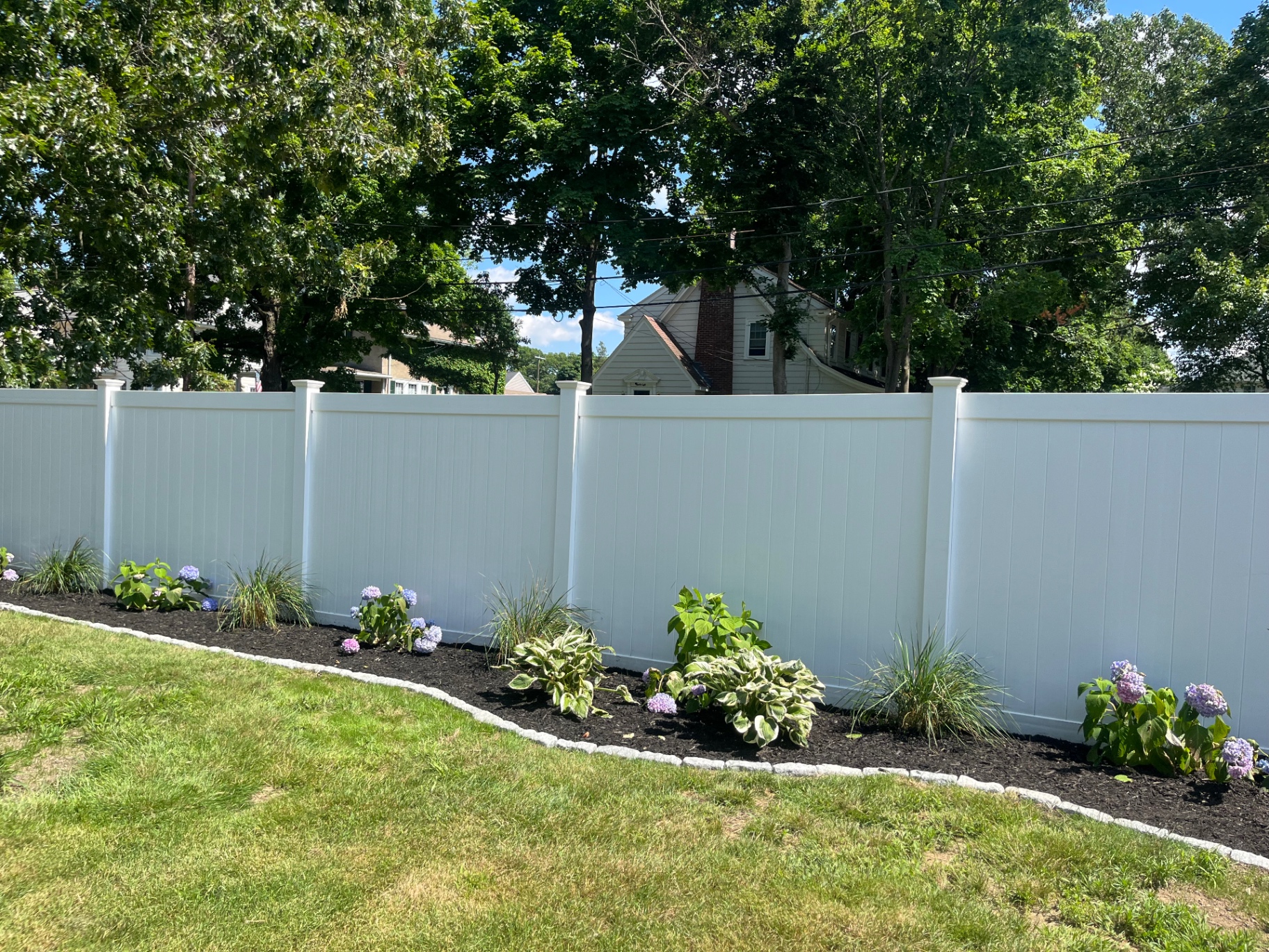 Curved planting bed along a white fence with hydrangeas and hostas