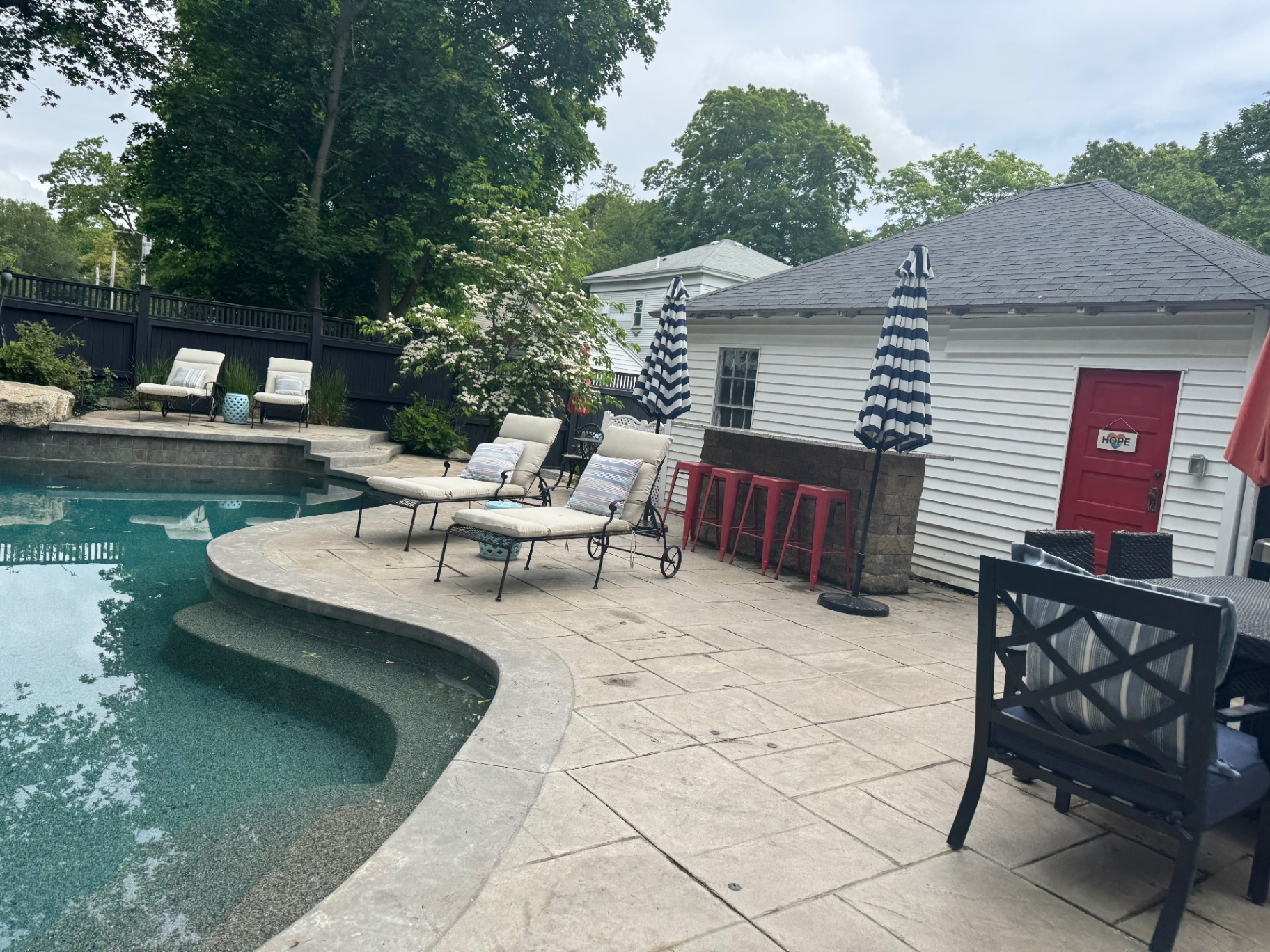 Poolside patio with outdoor bar, striped umbrellas, and pool house