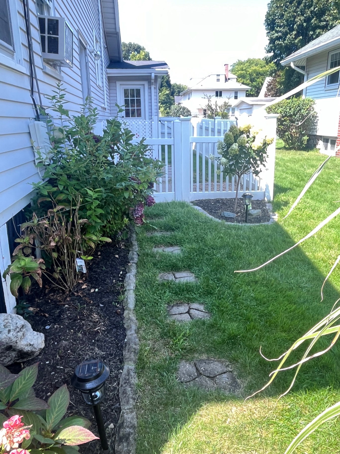 Side-yard stepping stone path beside a mulched bed and white fence gate